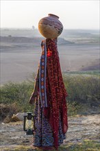 Ahir woman in traditional colorful clothes carrying water in a clay jug on her head