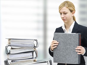 Thoughtful young businesswoman in front of a pile of folders