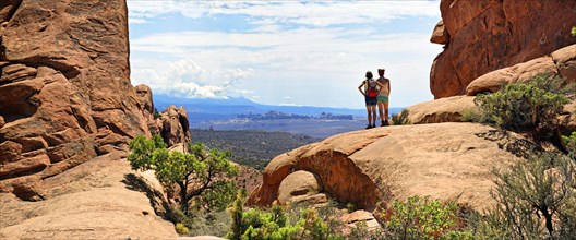 Hikers looking towards the La Sal Mountains from between red sandstone cliffs