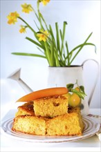 Carrot cake with a decorative carrot in front of daffodils