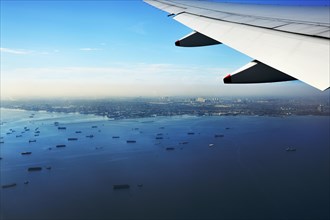 Wing of a plane and views of the port area of Jakarta on landing approach