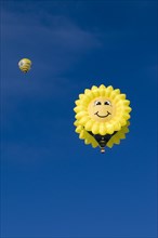 Hot air balloon in the shape of a 'laughing' sun or sunflower against a blue sky