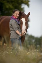 Woman standing next to a Hanoverian horse in a meadow