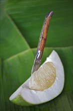 Pocket knife sticking in a segment of a pomelo fruit lying on a banana leaf