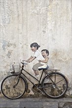 Bicycle in front of house wall with children painted as if they are riding the bike