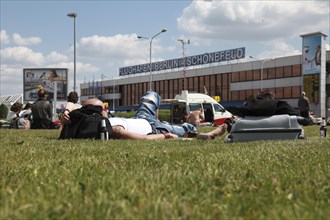 Passengers waiting for their flights on the lawn in front of the Berlin-Schoenefeld airport terminal building