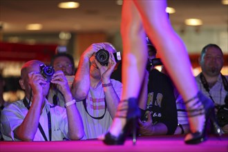 Visitors taking pictures of a model in high heel sandals at the Venus Erotic Fair