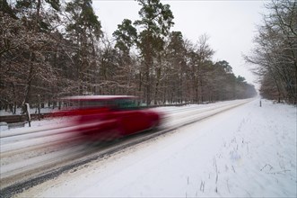 Snow-covered road in winter with a fast car passing