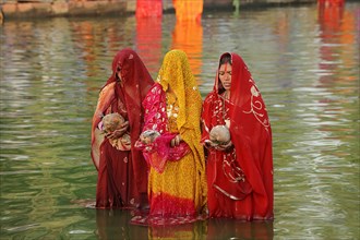 Women wearing saris with offerings standing in water during the Hindu Chhath Festival