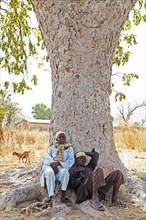 Two men wearing traditional Muslim clothing sitting under a tree