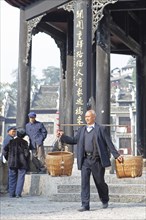 Man shouldering bamboo baskets in front of the Kuixingge Pagoda