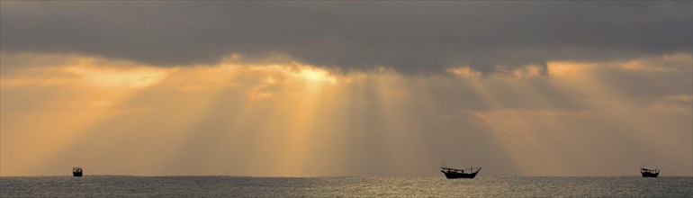 Sun beams above the Arabian Sea with the silhouettes of typical dhows