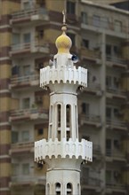 The minaret of a small mosque in front of an apartment building with balconies