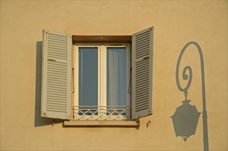 A facade in Ajaccio with a lone window and the shadow of a street lamp illuminated by warm morning light. Ajaccio is the capital of the mediterranean island of Corsica