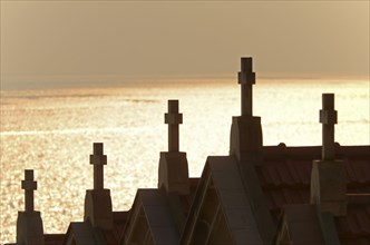 The silhouette of crucifixes of typical above-ground tombs in the cemetery of Ajaccio with the water of the mediterranean sea in the background. Ajaccio is the capital of the mediterranean island of C...