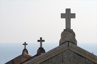 The silhouette of crucifixes of typical above-ground tombs in the cemetery of Ajaccio with the water of the mediterranean sea in the background. Ajaccio is the capital of the mediterranean island of C...