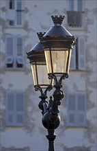 A street lamp illuminated by warm morning light in Ajaccio and the facades of houses in the background in shade. Ajaccio is the capital of the mediterranean island of Corsica