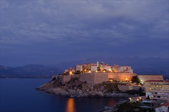 The citadel (castle) of Calvi surrounded by the mediterranean sea in front of the steep mountains of Corsica at the blue hour after sunset. Calvi is in the department Haute-Corse