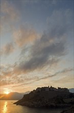 The silhouette of the citadel (castle) of Calvi surrounded by the mediterranean sea in front of a colorful sunrise. Calvi is in the department Haute-Corse
