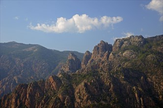 The typical rocky mountains of western Corsica near Evisa below a blue sky with a lone white cloud. Evisa illuminated by warm evening light surrounded by mountains. Evisa is in the department Corse-du...
