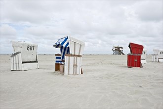 Roofed wicker beach chairs on the beach in front of a house on stilts