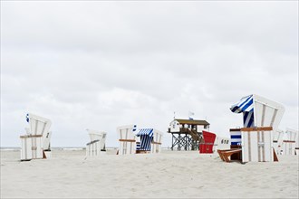 Roofed wicker beach chairs on the beach in front of a house on stilts
