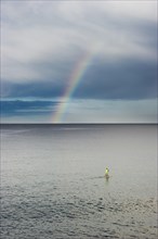 Stand up paddler with rainbow over the sea