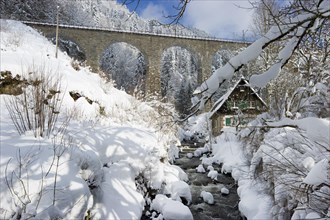 Snow-covered creek with a Black Forest house and a railway bridge