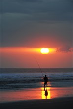 Fisherman fishing at sunset on the beach