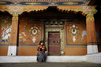 Young woman sitting in front of the ornate entrance of a side temple at the Paro Dzong