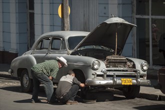Two men repairing a vintage car in a street of Cienfuegos
