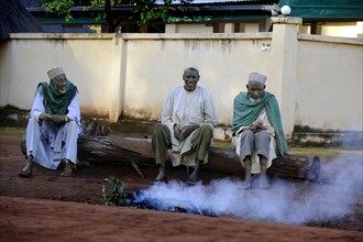 Three men sitting on the roadside in the village of Idool and supervising a fire