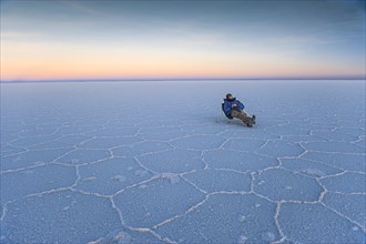 Man lying on a deck chair on the parched salt lake of Salar de Uyuni at dusk