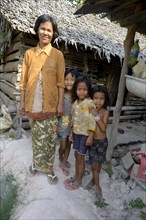 Woman standing with three girls in front of a hut made of wood and straw