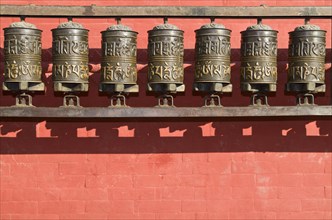 Buddhist prayer wheels in front of a red wall at Swayambhunath Stupa