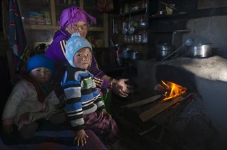 Nepali mother with her 2 children sitting at the fireplace in their kitchen
