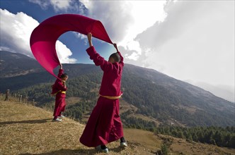 Young monks wearing red cloths flying kite with a blanket at a mountain slope