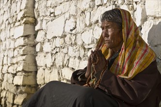 Old local woman praying in front of a brick wall