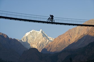 Cyclist crossing a suspension Bridge over Kali Ghandaki Valley