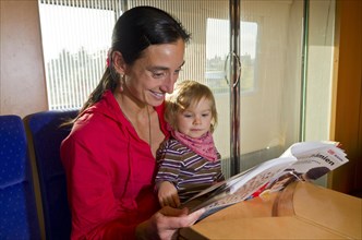 Young mother with child reading in a booklet inside ICE train