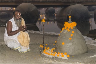 Priest praying at a shiva idol made of sand at the Sangam