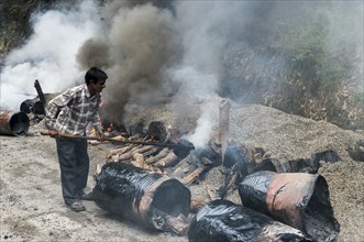 A worker mixing gravel and hot tar on open fires at a road construction site