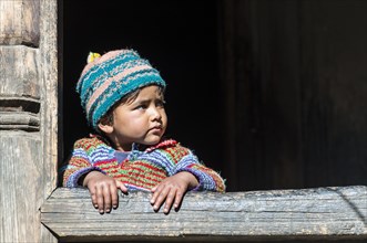 A small child looking out of the window of a wooden house