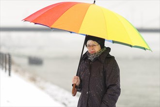 Woman standing with a colourful umbrella in winter on the bank of the Rhine River