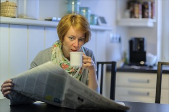 Woman sitting at the kitchen table reading the newspaper