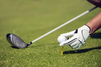 Hand with a glove putting a golf ball on a tee