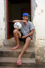 Teenager with football sitting in front of his home in a favela