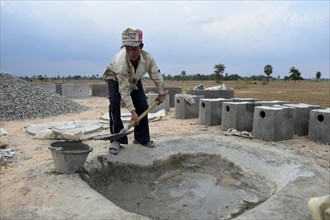 Young man in a local construction company mixing cement to produce parts for latrines