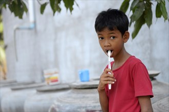 Young boy brushing his teeth outside a house
