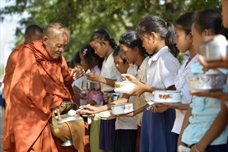 Children donating food and money to a Buddhist monk